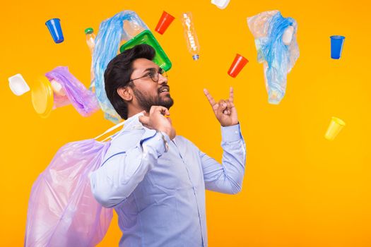 Environmental pollution, plastic recycling problem and waste disposal concept - surprised indian man holding garbage for recycling on yellow background