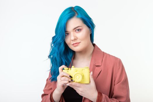 People, hobby and interests concept - Beautiful girl with blue hair hold yellow retro camera on white background