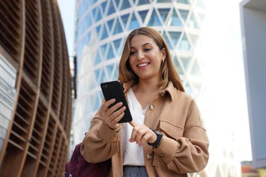 Young business woman walking in modern sustainable city using mobile phone