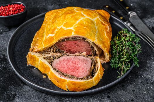Beef Wellington classic steak dish with tenderloin meat on a plate. Black background. Top view
