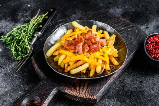 Delicious golden French fries with melted cheddar cheese and bacon. Black background. Top view