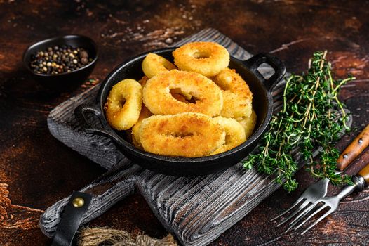 Fried squid rings breaded on a cutting board. Dark background. Top view