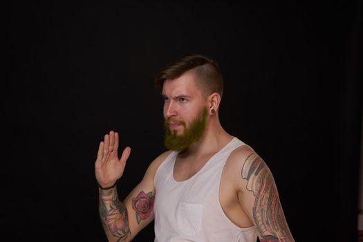 bearded man with tattoos on his arms gesturing with his hands dark background. High quality photo
