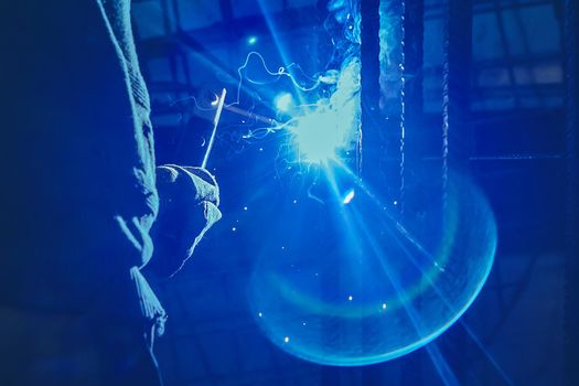 Working man is doing welding work on metal structures in a factory or industrial enterprise