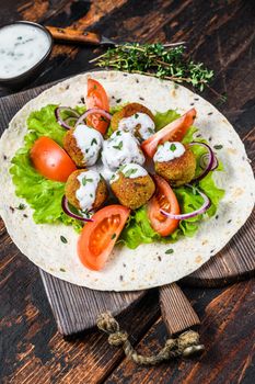 Vegetarian falafel with vegetables and tzatziki sauce on a tortilla bread. Dark wooden background. Top view