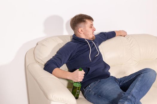 Depression and alcoholism concept - aggressive young man sitting on a sofa with bottle of alcohol