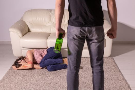 Alcoholism, abuse and domestic violence - Woman lying on the floor, afraid of men with bottle