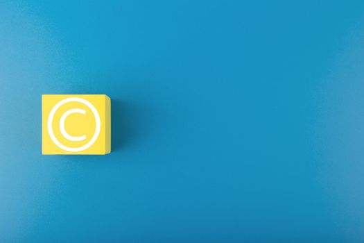 Minimal blue copyright protection concept on blue background with copy space, copyright symbol on yellow cube