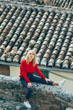 Young blond woman sitting near beautiful roofs of charming old houses.