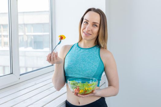 Healthy lifestyle, fitness and diet concept - dietary salad and slim woman in sports wear near window