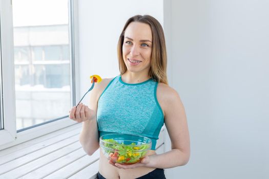 Healthy lifestyle, fitness and diet concept - dietary salad and slim woman in sports wear near window