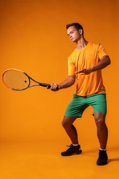 Full-length portrait of a tennis player man in action against orange background