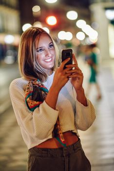 Woman taking photograph with smartphone at night in the street