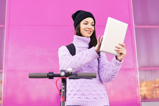 Woman in her twenties with electric scooter using digital tablet outdoors.