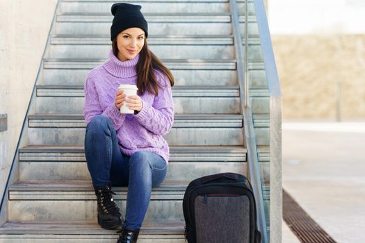 Woman in her twenties taking a coffee break sitting on some steps in the street.