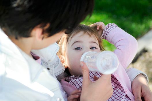 Baby girl drinking milk from baby bottle. Mother feeding daughter from bottle.
