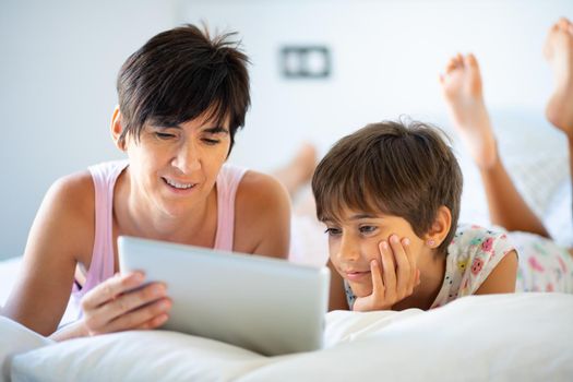 Middle-age mother with her eight years daughter using digital tablet in bedroom.