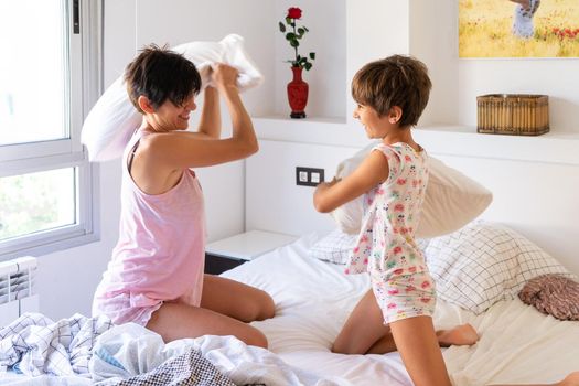 Mother and daughter having funny pillow fight on bed.