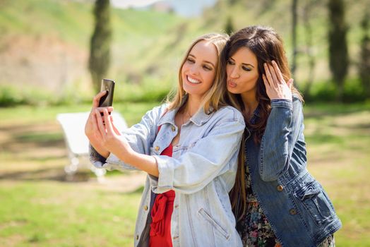 Two young women taking a selfie photograph in urban park