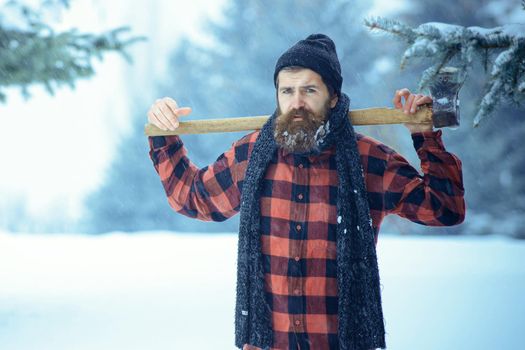 Hipster lumberjack man in snowy cold forest. Winter man with beard hold axe.