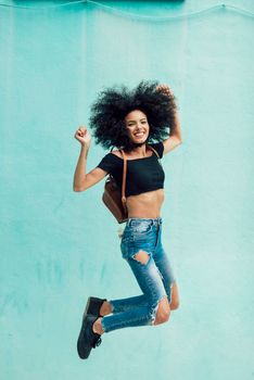 Young mixed woman with afro hair jumping outdoors.
