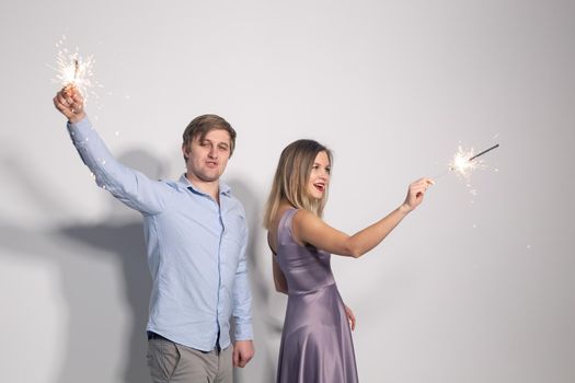 Party, event and holiday concept - man and woman fooling around with sparklers over grey background
