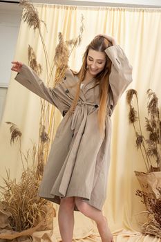 pretty woman in beige raincoat on pastel fabric background. fashion photo shoot