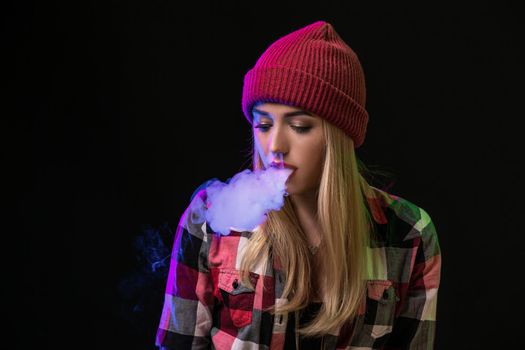 Vaping girl. Young hipster woman vape e-cig on studio on black background. Hip-hop style. Close up.