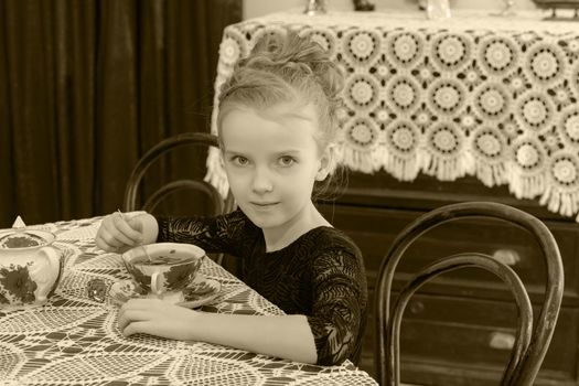 Beautiful little girl drinking tea at the table.