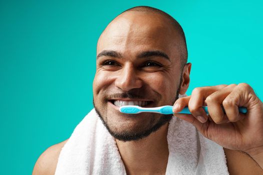 Cheerful dark-skinned male brushing his teeth against turquoise background