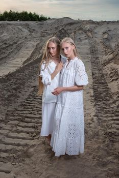 two attractive young twin sisters posing at sand quarry in elegant white clothes