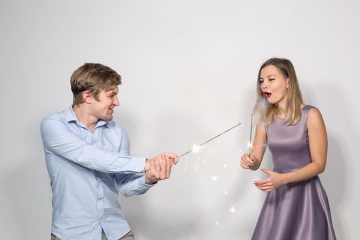 Holidays, party and celebrations concept - young funny happy couple with sparklers fooling around on white background