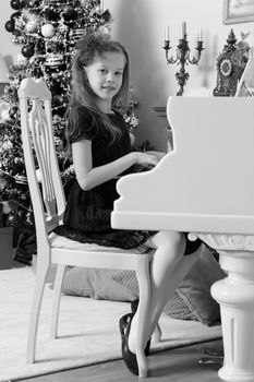 Beautiful, elegant little girl holding hands on the keys of a white Grand piano. Girl playing at the Christmas concert in the music school.Black-and-white photo. Retro style.