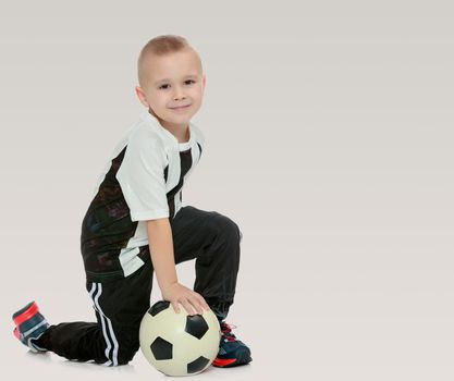 Cute little boy with the ball.The boy squats and holds the ball with his hands.On a gray background.