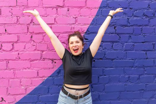 Cheerful positive young woman in goth clothing posing against a blue-purple brick wall. The concept of positive advertising content.