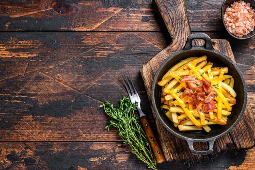 French fries with melted mix of cheddar cheese and bacon served in a pan. Dark wooden background. Top view. Copy space