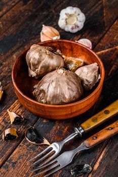 Bulbs and cloves of fermented black garlic in a plate. Dark wooden background. Top view