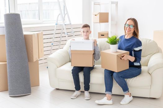 Cute single mom and little boy son sort boxes with things after the move. The concept of housewarming mortgage and the joy of new housing.