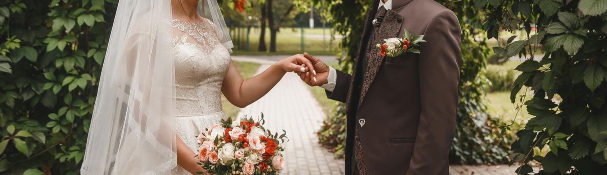 The groom in a brown suit holds the bride's hand with a wedding bouquet.