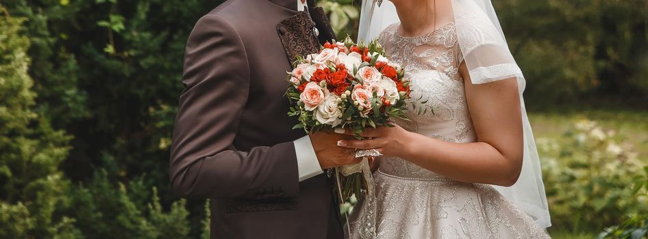 The bride and groom hold together with their hands a wedding bouquet of flowers.