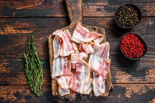 Raw pork bacon meat slices on a wooden cutting board. Dark wooden background. Top view