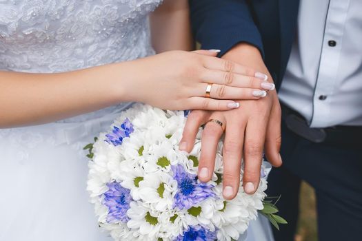 Tenderness and weasel hands of the bride and groom on the wedding bouquet of flowers
