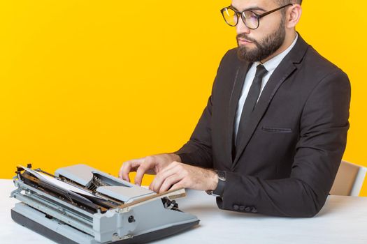 Side view of a young charming male businessman in formal attire and glasses typing on a typewriter text. Concept of business affairs and ideas.