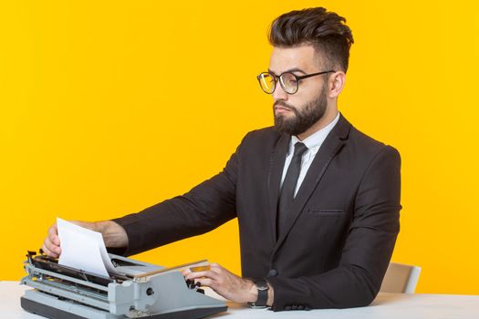 Side view of a young charming male businessman in formal attire and glasses typing on a typewriter text. Concept of business affairs and ideas.