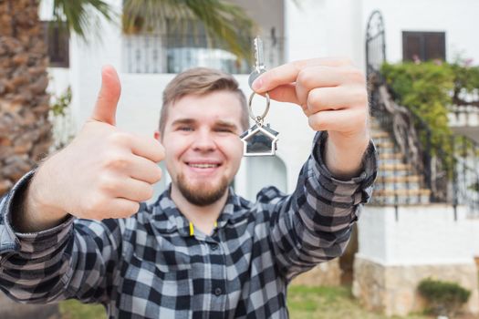 Property, ownership, new home and people concept - young man with keys standing outside new home