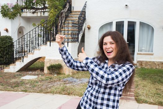 New home, house, property and tenant - Young funny woman holding key in front of her new home after buying real estate