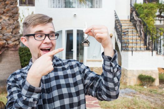 Dwelling, buying home, real estate and ownership concept - handsome man showing his key to new home