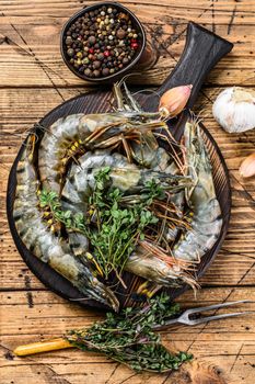 Raw black tiger shrimps prawns on a cutting board with herbs. wooden background. Top view