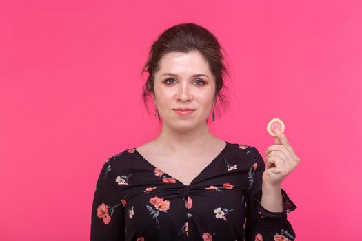 Safe sex, health and contraception concept - woman holding in hands a condom on pink background
