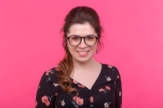 Portrait of a smart charming brown-eyed young positive woman in eyeglasses posing on a bright pink background